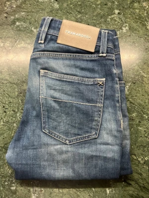 Blå jeans från Tramarossa - Tramarossa Leonardo Buttons i mörkblå säljes. Jeansen är välanvända men har mycket kvar att ge, har fått naturlig fade.  Slitning finns vid mobilfickan på höger sida (se bild). Otroligt mjuka och väldigt sköna att bära. Vita kontrastsömmar som ger en stilren touch.       Modell: Leonardo Buttons                                                 Storlek: 30, passar mig som är 180cm.                          Nypris: Ca 3500kr