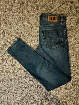 Mörkblå jeans från Diesel - Snygga mörkblå jeans från Diesel med klassisk femficksdesign och brunt läderpatch med logga bak i midjan. Jeansen har raka ben och kontrastsömmar i orange. Perfekta för dig som gillar stilrena och tidlösa denimplagg. W30 L34