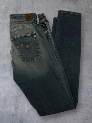 Gråblå jeans från Replay - Snygga gråblå jeans från Replay med klassisk femficksdesign och diskreta slitningar. Jeansen har raka ben och detaljerade sömmar på bakfickan. Tillverkade i mjuk denim som ger en skön passform och cool look.