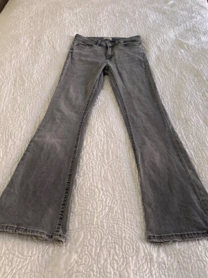 Grå bootcut jeans - Säljer ett par grå bootcut jeans med råa, fransiga benslut och klassisk femficksmodell. Jeansen har en snygg tvättad look och är perfekta för dig som gillar en avslappnad men trendig stil. Materialet är mjukt denim som sitter skönt hela dagen.