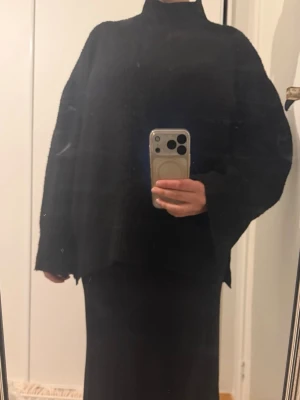 Oversized svart stickad polotröja - Säljer en oversized svart stickad polotröja med breda ärmar och hög krage. Tröjan har en lös passform och är ribbstickad vilket ger en snygg struktur. Perfekt för lager på lager och riktigt mysig under kalla dagar.