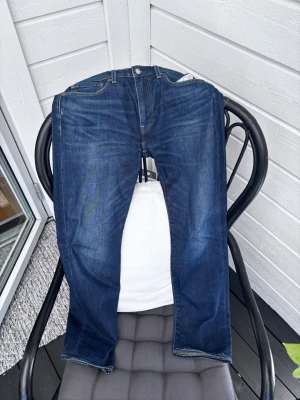 Levi's 502 mörkblå jeans W32 L32 - Säljer ett par klassiska Levi's 502 jeans i mörkblå denim. Modellen har rak passform och fem fickor. Snygga kontrastsömmar och ikonisk läderpatch bak i midjan. Perfekta till en avslappnad streetwear-look.