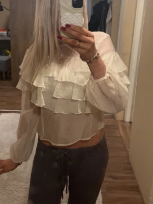  blus med volanger - Söt blus i ljusbeige med flera lager volanger framtill. Blusen har långärmade, väldigt fin och ha på sommaren. Perfekt för dig som gillar en trendig och feminin stil.