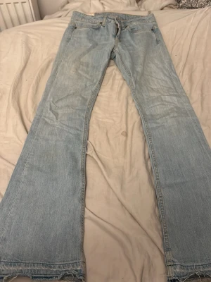Ljusblå bootcut jeans från dondup  - Säljer ett par ljusblå bootcut jeans från dondup med råa, fransiga benslut och klassiska fem fickor. Jeansen har en avslappnad passform och är tillverkade i denim. Perfekta för en casual och trendig look.