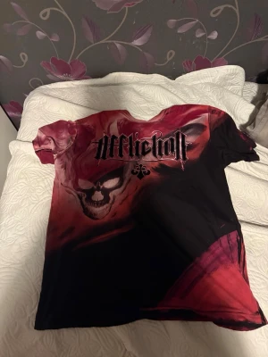Affliction t-shirt  - Säljer en kortärmad t-shirt från Affliction med stort dödskalletryck och logga på bröstet. T-shirten har en cool mix av svart och röd färg, och är gjord i mjuk bomull. Perfekt för dig som gillar edgy och unika plagg.