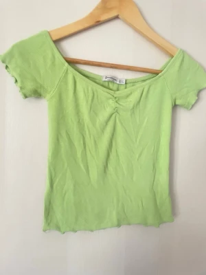 Limegrön topp Stradivarius XS off shoulder  - snygg limegrön topp från Stradivarius i storlek XS Trendigt off shoulder-liknande snitt med korta ärmar och fin rynkning framtill som ger en flattering passform. Ribbat material som sitter snyggt på kroppen.  Perfekt statement-plagg som lyfter vilken outfit som helst 💚