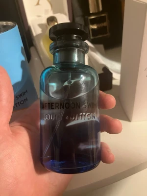 Louis Vuitton Afternoon Swim parfym - Exklusiv parfym från Louis Vuitton, Afternoon Swim, i en elegant blå glasflaska med svart lock. Flaskan har en modern, rundad form och texten är ingraverad i glaset. Doften är känd för sina fräscha och citrusaktiga noter. Perfekt för dig som gillar lyxiga parfymer. Full presentation + kvitto finns 
