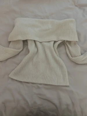 Off shoulder stickad tröja XS - Säljer en off shoulder stickad tröja i krämvit färg. Tröjan har bred ribbstickning och långa ärmar, perfekt för att skapa en trendig och avslappnad look. Materialet är mjukt och stretchigt, vilket gör den bekväm att bära.