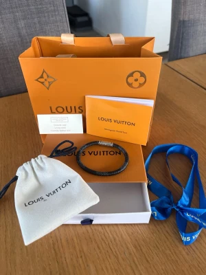Elegant Louis Vuitton Armband - Snyggt äkta mörkblått armband från Louis Vuitton med graverat ”louis vuitton” på magneten och en väldigt elegant design. Kommer med originalpåse, ask och band. Perfekt accessoar för dig som gillar exklusiva detaljer och vill sticka ut med något från ett lyxigt märke.