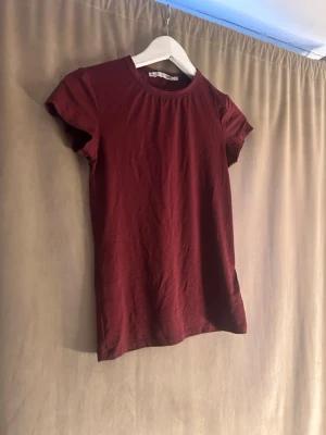 Vinröd t-shirt från 157 - En enkel och stilren vinröd t-shirt från 157 med rund hals och korta ärmar. Tillverkad i mjuk bomull som känns skön mot huden. Perfekt basplagg att matcha med jeans eller kjol.