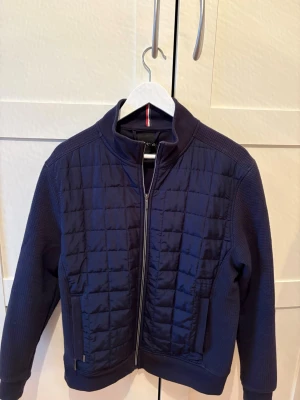 Marinblå quiltad jacka - Snygg marinblå jacka med quiltad front och dragkedja. Jackan har ribbade ärmar och sidor, ståkrage och två fickor framtill. Perfekt för dig som vill ha en stilren och sportig look.                            Priset är inte hugget i sten så hör gärna av er med ett förslag:)