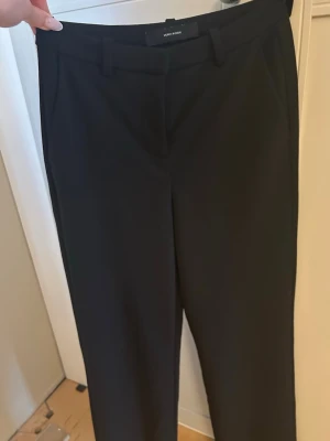 Svarta kostymbyxor från Vero Moda - Stilrena svarta kostymbyxor från Vero Moda med raka ben och klassisk passform. Byxorna har hällor för skärp och diskreta sidofickor. Perfekta för en dressad look. Materialet känns mjukt och följsamt.