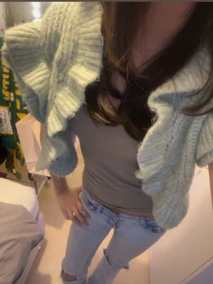 Ljusgrön stickad bolero med volanger - Supersöt ljusgrön stickad bolero med stora volangärmar och kort passform. Mjuk och chunky stickning i ett fluffigt material, perfekt för att slänga över ett linne eller t-shirt. Ger en trendig och cozy vibe till din outfit.