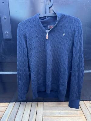 Mörkblå kabelstickad tröja Morris🙌🤩 - Snygg mörkblå kabelstickad tröja från Morris med dragkedja framtill och diskret logga på bröstet. Tröjan har ribbade muddar och klassisk passform. Perfekt för lager på lager och stilrena outfits. Liten defekt som visas på bilden🙌🤩