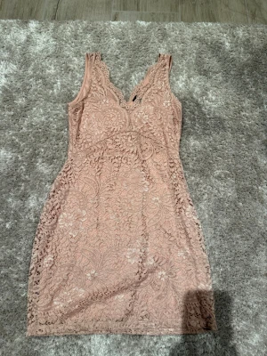 Rosa spetsklänning från Vero Moda - Supersöt rosa spetsklänning från Vero Moda i kort modell. Klänningen har v-ringning, är ärmlös och täckt med vacker spets med blommigt mönster. 