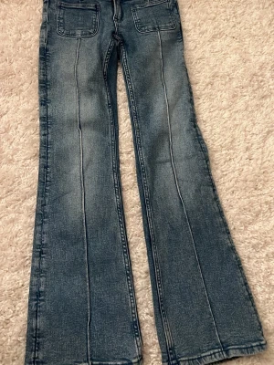 Blå bootcut jeans  - Säljer ett par blå jeans med utsvängda ben och markerade sömmar framtill. Jeansen har stora fyrkantiga fickor fram och dubbla knappar i midjan. 