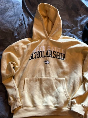 Tre hoodies i gult och vinrött beige  - Säljer tre hoodies: en ljusgul med trycket 'Track & Field Scholarship' och en varg-logga på bröstet, samt en enkel vinröd hoodie utan tryck. En beige. Alla 3 har stor känguruficka framtill och huva. Perfekta för chill dagar eller när du vill vara bekväm. Skavanker förekommer. Dom är oversized i storlekarna M-Xl