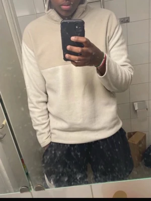 Beige och vit fleece halvzip tröja - Mysig fleece tröja i beige och vitt med halvzip och hög krage. Perfekt för kyliga dagar och enkel att matcha med olika outfits. Tröjan har en avslappnad passform och är tillverkad i mjukt fleecematerial.