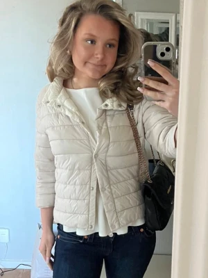 Ljusbeige trekvartsärmad dunjacka - Säljer en trekvartsärmad ljusbeige dunjacka från Amisu med kortare passform och horisontella sömmar. Jackan har tryckknappar framtill och en hög krage. Perfekt för vår/sommar och lätt att styla med olika outfits. 