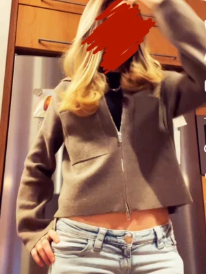 Brun zipcardigan - Snygg beige zipcardigan från Åhléns med två stora fickor framtill och krage. Tröjan är croppad och har långa ärmar. Perfekt att styla med jeans eller kjol för en chill look. Nypris 599kr