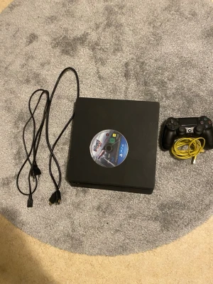PlayStation 4 Slim med handkontroll - Säljer en svart PlayStation 4 Slim från Sony med tillhörande svart DualShock 4-handkontroll, strömkabel, HDMI-kabel och spelet Need for Speed Rivals på skiva. Konsolen har sopren design i matt plast och passar perfekt för gamingkvällar.