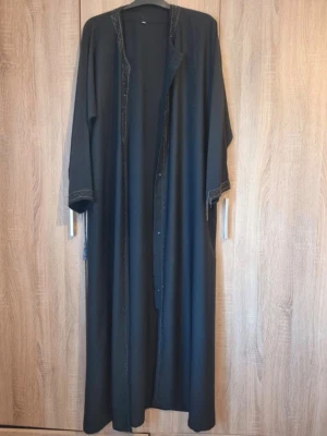 Svart öppen abaya  - En fin svart/blå öppen abaya med sten delatljer. Knappar finns bara på en sida så går inte att stänga, men är fortfarande väldigt fin öppen. Den är ca 145 cm lång💕Skriv om du har frågor🥰