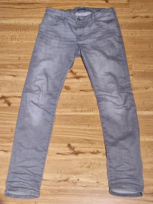Grå slim fit jeans från Scotch & Soda - Snygga grå slim fit jeans från Scotch & Soda med klassisk femficksdesign. Jeansen har raka ben och patch med logga bak i midjan. Perfekta för en trendig och avslappnad look.