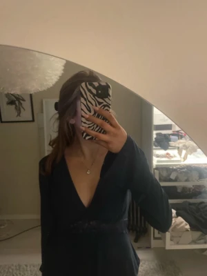 Marinblå långärmad topp med spets - Snygg marinblå klänning med lång ärm och djup v-ringning. Klänningen har en fin spetsdetalj i midjan som ger en extra touch. Perfekt för dig som vill ha en elegant och stilren look. Aldrig använd