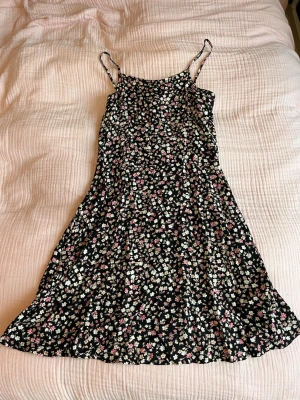 Blommig klänning - Söt vit och rosa blommig klänning med svart grund. Jätteskönt material med tunna straps och stretch i ryggen