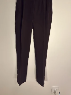 Bruna kostymbyxor Vero Moda - Snygga bruna kostymbyxor från Vero Moda i storlek 36. Byxorna har raka ben, pressveck och diskreta sidofickor. Perfekta för en clean och stilren look. Materialet känns mjukt och följsamt, vilket gör dem bekväma att bära hela dagen.