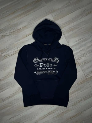 Marinblå hoodie från Polo Ralph Lauren - Snygg marinblå hoodie från Polo Ralph Lauren med stor vit logga och text på bröstet🤗 använd ett par gånger men inga fel på den🙌🏻 inget äkthetsbevis tyvärr. Hör av er vid snabbaffär samt funderingar🤩