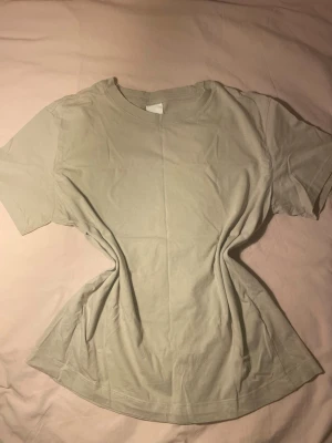 Beige basic t-shirt från H&M - En enkel och stilren beige t-shirt från H&M Basics. T-shirten har rund halsringning och korta ärmar, tillverkad i mjuk bomull. Perfekt att matcha med jeans eller shorts för en avslappnad look.