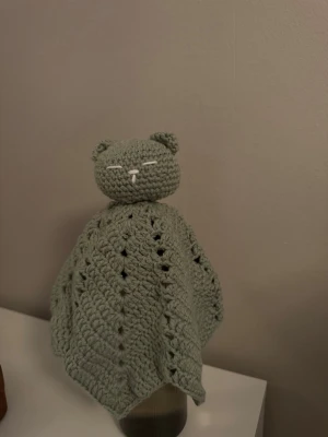 Grön virkad snuttefilt katt - Söt handvirkad snuttefilt i form av en björn med rundat huvud, små öron och broderat ansikte. Filten är ljusgrön och har ett luftigt mönster. Perfekt som mysig kompis eller dekoration.