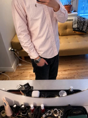 Rosa och vit randig skjorta Polo Ralph Lauren - Säljer en klassisk rosa och vit randig skjorta från Polo Ralph Lauren med broderad logga på bröstet. Skjortan har lång ärm, knappar framtill och button-down krage. Tillverkad i mjuk bomull och passar perfekt till jeans eller chinos.