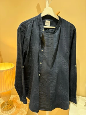 Mörkblå henley-skjorta från Zara - Snygg mörkblå henley-skjorta från Zara med subtilt randigt mönster och relaxed fit. Skjortan har knappar framtill och lång ärm, perfekt för en chill och stilren look.