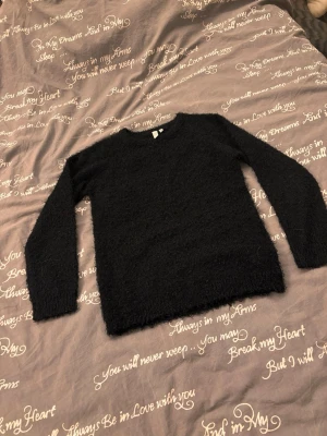 Svart fluffig stickad tröja - Mysig svart stickad tröja med fluffig textur och lång ärm. Perfekt för kyliga dagar och enkel att matcha till olika outfits. Klassisk rund hals sopm ger en clean look.