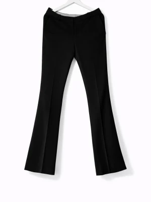 Svarta utsvängda kostymbyxor - Snygga svarta kostymbyxor med utsvängda ben och pressveck. Byxorna har hällor för skärp, fickor bak och klassisk midja. Perfekta för en stilren och trendig look. Finns lagning i skrevet, se bild