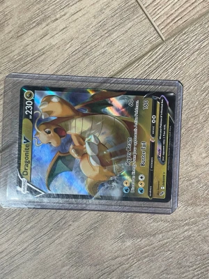 Pokémonkort Dragonite V - Säljer ett Pokémonkort med Dragonite V, 230 HP. Kortet har en holografisk yta och är skyddat i plastficka. Färgerna är främst guld, blått och grönt med Dragonite i fokus. Perfekt för samlare eller Pokémonfans.