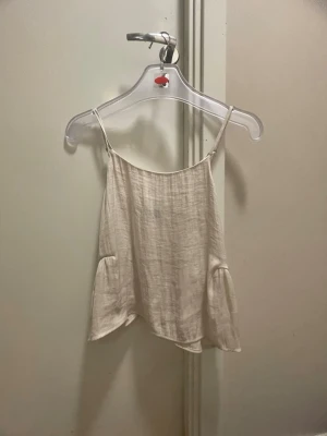 Vit linnetopp från Gina Tricot - Säljer en ljusvit linnetopp från Gina Tricot med tunna axelband och avslappnad passform. Toppen har en lätt struktur i tyget och är perfekt för varmare dagar. Enkel och stilren design som är lätt att matcha.