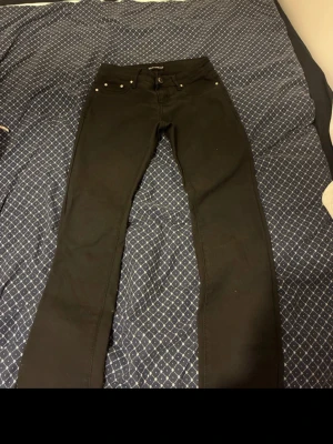 Svarta jeans från Dolce & Gabbana - Säljer ett par svarta jeans från Dolce & Gabbana med klassisk femficksmodell och raka ben. Jeansen har snygga metallknappar och detaljer, samt bälteshällor i midjan. Perfekta för dig som gillar stilrena och exklusiva plagg. För kvinna säljer även på vinted 