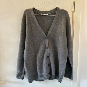 Grå kofta från Zara med knappar - Mysig grå kofta från Zara med djup V-ringning och knäppning framtill. Långa ärmar och ribbade muddar vid ärmslut och nederkant. Storlek S. Aldrig använt💛