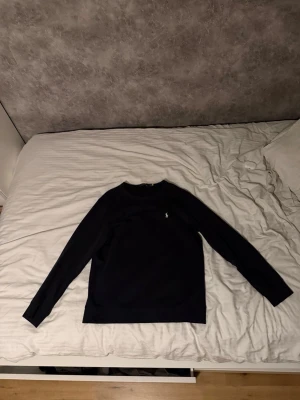 Mörkblå långärmad tröja från Polo Ralph Lauren - Snygg mörkblå tröja från Ralph Lauren med klassisk rund halsringning och den ikoniska logotypen broderad på bröstet. Tröjan har långa ärmar och är perfekt för lager på lager. Pris kan diskuteras