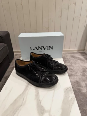 Svarta sneakers från Lanvin - Snygga svarta sneakers från Lanvin med glansig lackad tå och svarta skosnören. Skorna är i grymt skick och är i storlek 44 (11). Skorna passar även om man har storlek 45!