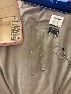 Smyckeskit med ringar, halsband & örhängen - Säljer ett kit med flera silvriga smycken: sex ringar med olika motiv, ett halsband med berlocker, ett armband med pärlor och öga samt två par örhängen från Edblad och Montini. Perfekt för dig som gillar att mixa och matcha accessoarer.
