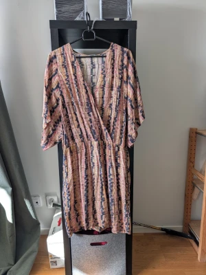 Mönstrad omlottklänning Filippa K - Säljer en snygg omlottklänning från Filippa K i storlek L. Klänningen har ett färgstarkt randigt mönster i rosa, beige, blått och svart, med v-ringning och korta ärmar. Perfekt för dig som gillar unika plagg med skön passform.