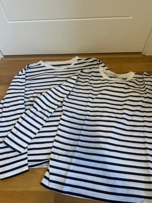 Randiga långärmade tröjor från 157 - Två klassiska långärmade tröjor från 157 med marinblå och vita ränder. Båda har rund halsringning och raka ärmar. Perfekta att styla med jeans eller kjol för en enkel och snygg look.