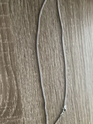 Silvrigt kedjehalsband - Snyggt och stilrent halsband i silverfärgad metall med tunn kedja och klassiskt lås. Perfekt för att addera en enkel men elegant touch till din outfit. Passar bra att bära ensamt eller att kombinera med andra halsband för en lager-på-lager-look.