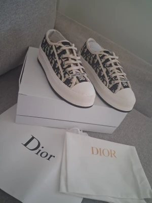 Dior Oblique låga sneakers - Snygga Dior Oblique sneakers i lågt snitt med beige och svart monogrammönster. Skorna har vita snören, gummisula och tåhätta samt detaljer med 'Christian Dior' på plösen och tån. Perfekta för dig som vill ha en exklusiv och trendig look.