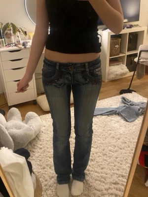 Lågmidjade blå bootcut jeans - Säljer ett par blå lågmidjade straight/skinny jeans köpta från Sellpy med dekorativa detaljer på fickorna. Jeansen har en klassisk femficksmodell och är tillverkade i denim med snygg tvätt. Midjemått 34x2 cm innerbenslängden 79 cm gren 17 cm💙skriv gärna frågor och pris kan diskuteras!💗