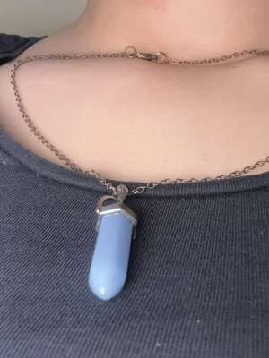 Halsband med blå kristallhänge - Snyggt halsband med en kedja i silverfärg och ett blått kristallformat hänge. Kristallet lyser i mörkret efter att den har fått ljus på sig. Anledningen t att jag säljer den är pga att detta är inte min stil.